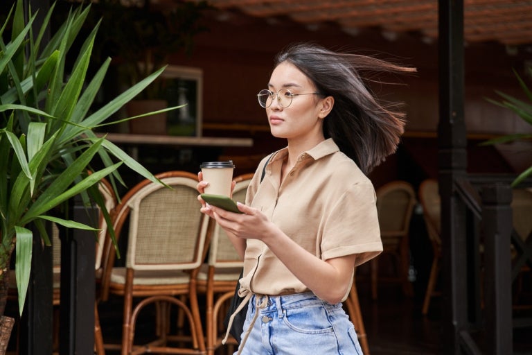 A woman holding her drink and phone while walking outside
